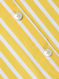 Close-up of the Cosette Shirt, a tailored piece made from organic cotton in yellow and white vertical stripes, featuring two shiny silver buttons engraved with text and sewn on with yellow thread.