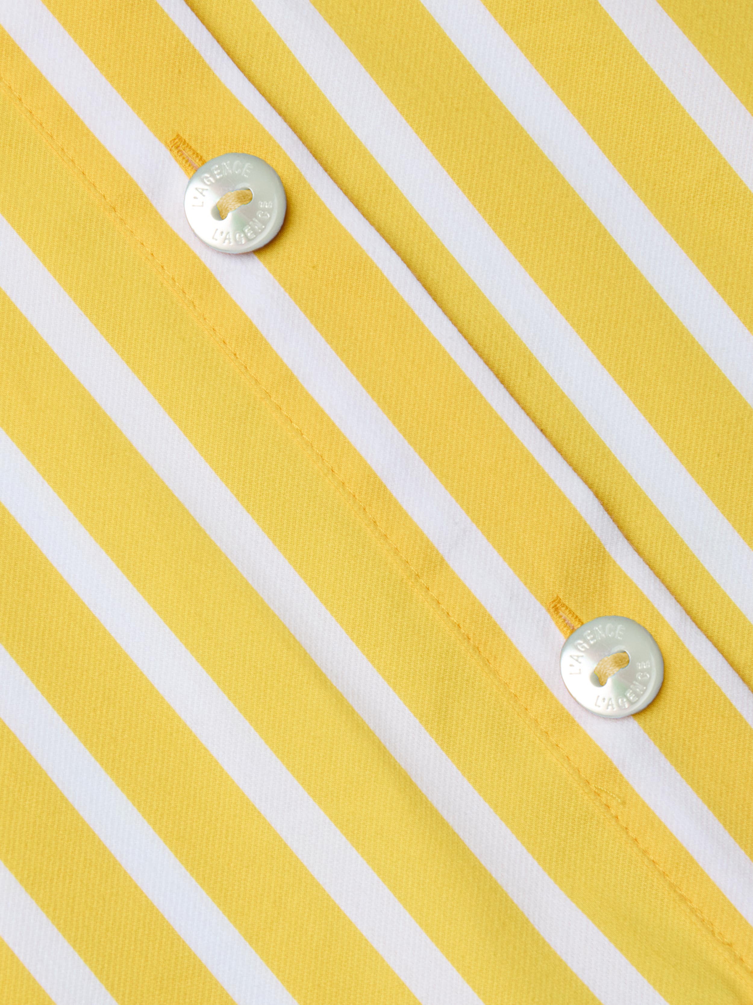 Close-up of the Cosette Shirt, a tailored piece made from organic cotton in yellow and white vertical stripes, featuring two shiny silver buttons engraved with text and sewn on with yellow thread.