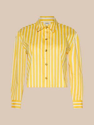 The Cosette Shirt is a classic tailored long-sleeve shirt with vertical yellow and white stripes, a pointed collar, and a straight hem, made from organic cotton-blend poplin and shown on a beige background.