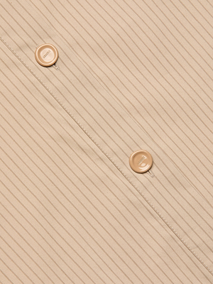Close-up of the Cosette Shirt in beige fabric with thin vertical stripes and two beige buttons sewn along a seam, positioned diagonally across the image.