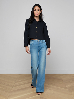 A woman wears the Cosette Shirt, a tailored black top with a cropped hem, paired with blue jeans.