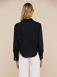 A person with long blonde hair models the Cosette Shirt in black, paired with blue jeans and shown from the back against a plain light background.