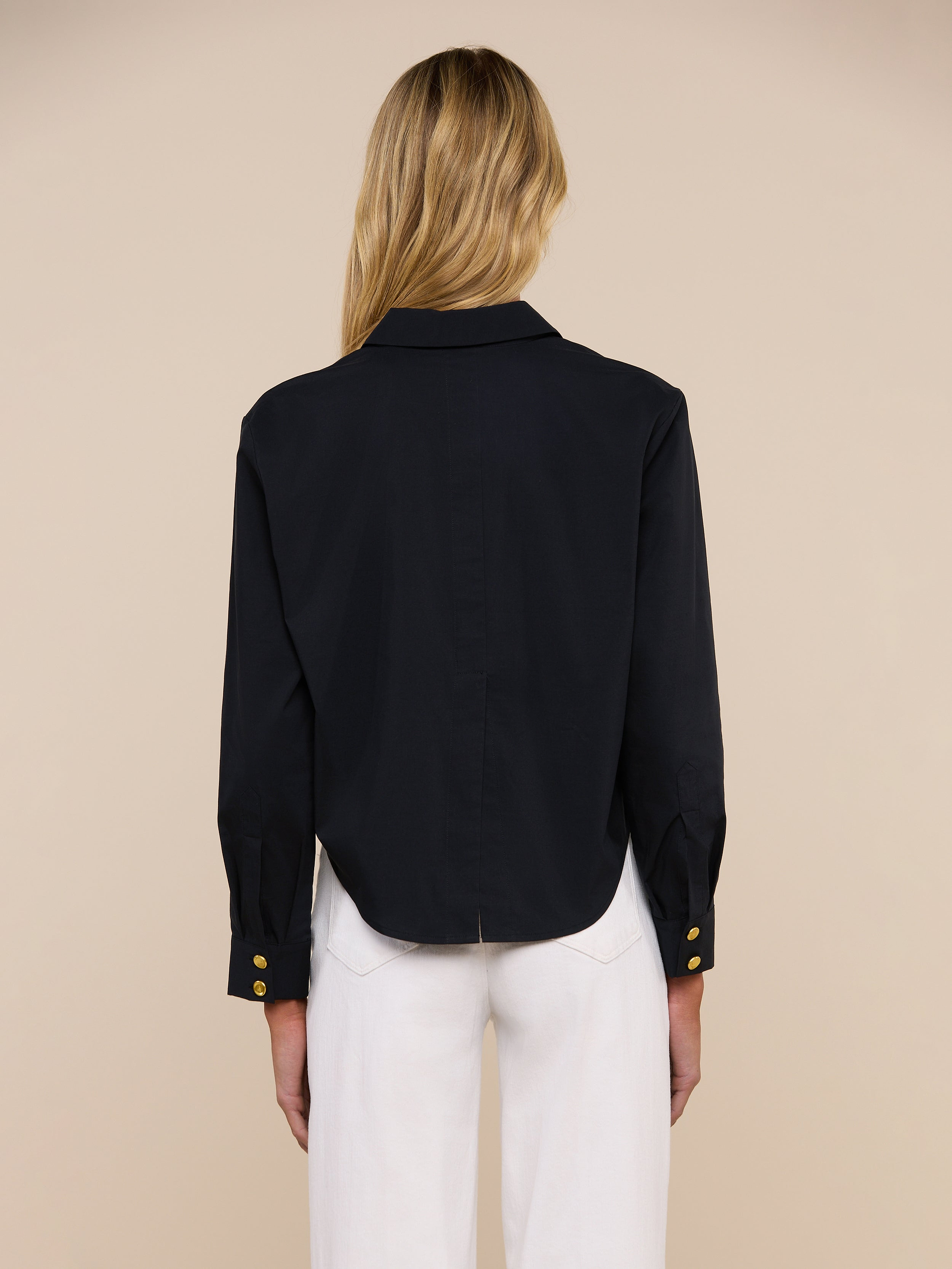 A person with long blonde hair models the Cosette Shirt in black, paired with blue jeans and shown from the back against a plain light background.