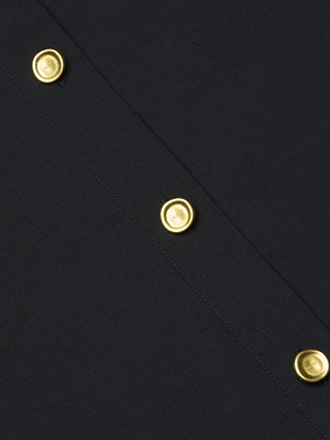 Close-up of the Cosette Shirt, a black tailored piece with a diagonal seam adorned by four evenly spaced shiny gold buttons.