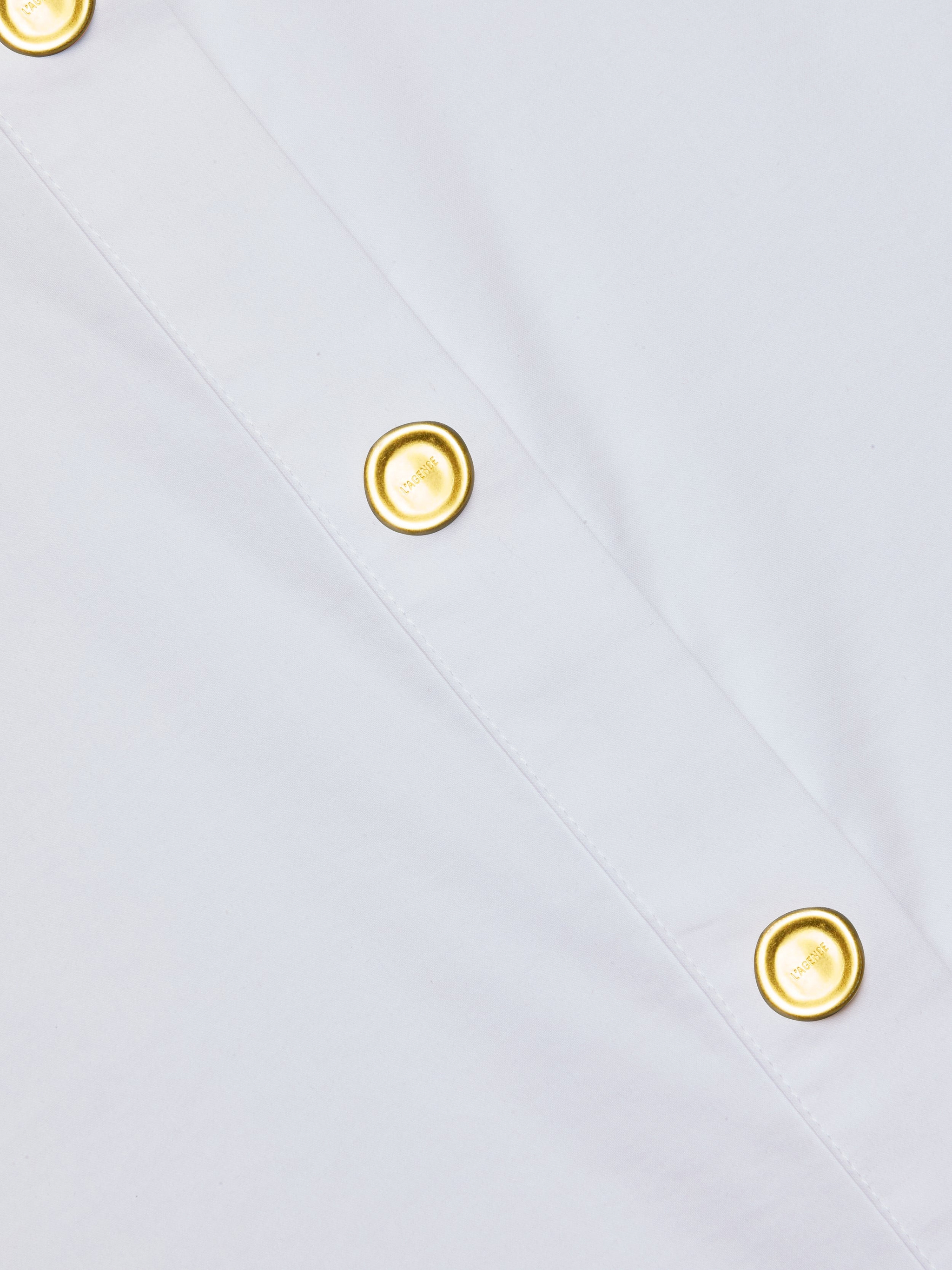 Close-up of the Cosette Shirt, a white poplin design featuring two gold-colored buttons aligned along a diagonal seam.