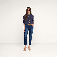A woman stands against a plain white background, hands in pockets and looking forward, wearing sunglasses, blue jeans, beige heels, and the Cosette Shirt in navy.