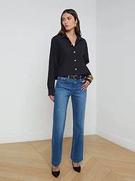 A woman stands against a plain white background wearing the Cosette Shirt, styled with blue jeans, a black belt, black heels, and large hoop earrings.