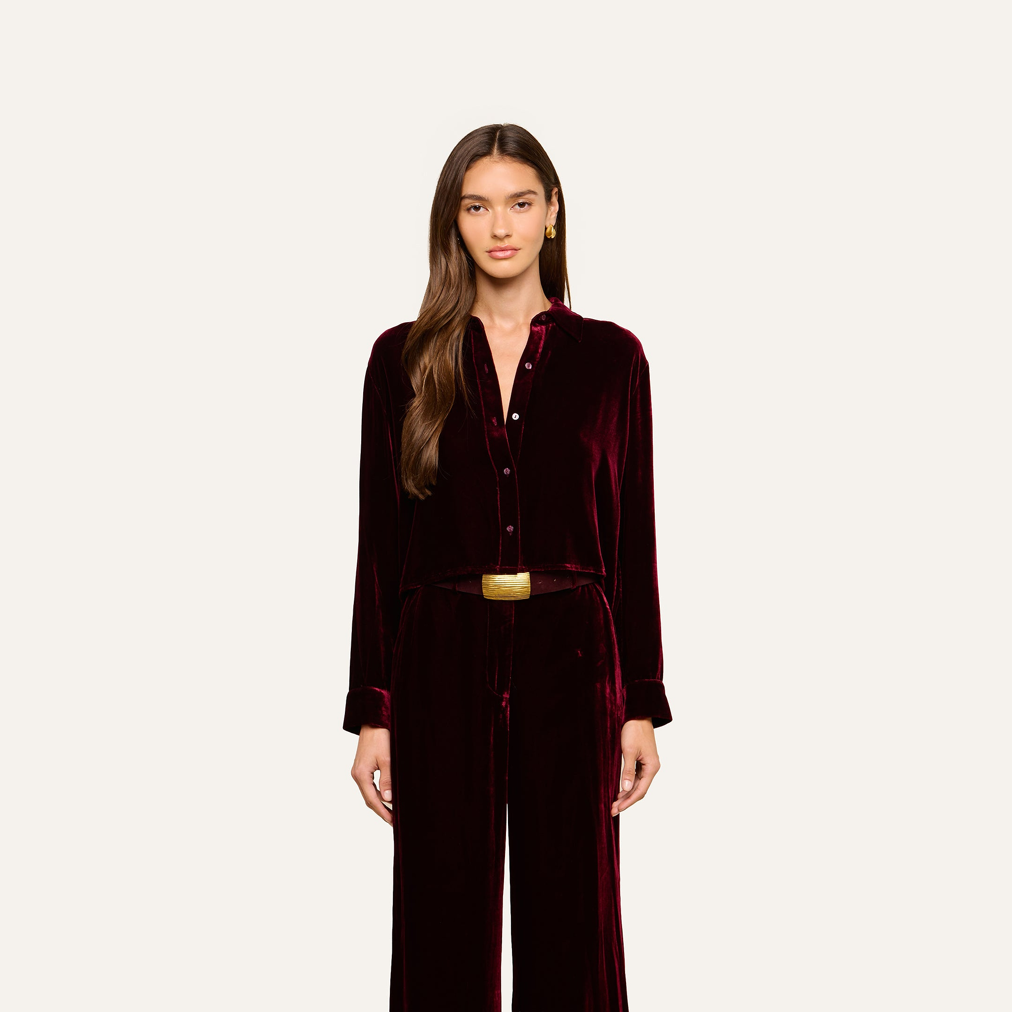 A woman stands facing forward against a plain light background, wearing the Cosette Velvet Shirt in burgundy, paired with matching wide-leg pants and a belt.