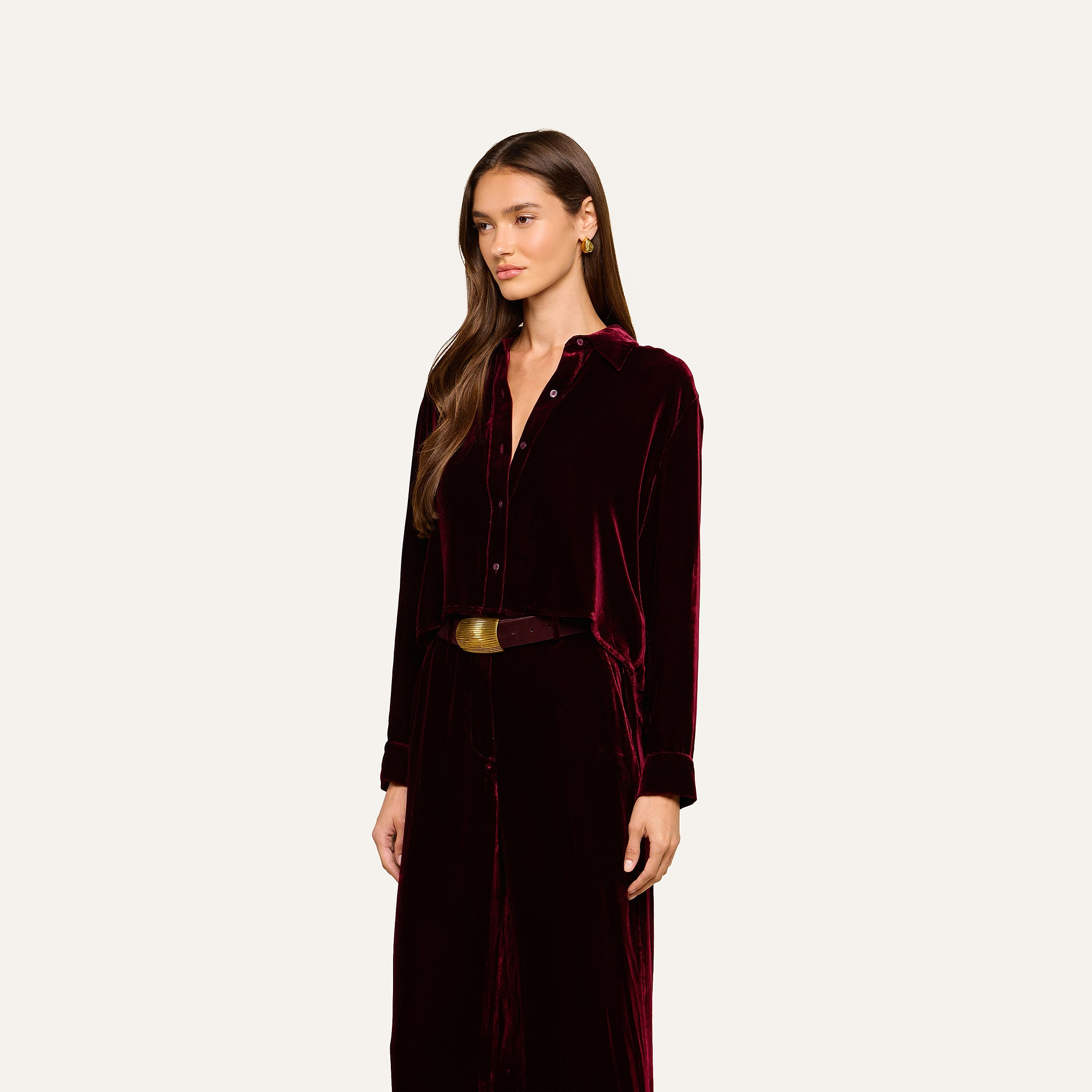A woman wearing the Cosette Velvet Shirt, a long-sleeved dark red velvet dress with buttons and a wide belt, stands against a plain light background.