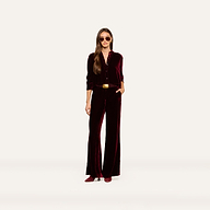 A woman stands against a plain white background with one hand in her pocket, wearing the Cosette Velvet Shirt styled as a jumpsuit, along with matching shoes, sunglasses, and a belt.
