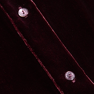 Close-up of the Cosette Velvet Shirt in dark red, featuring two silver snap buttons along a seam and highlighting the luxurious texture and sheen of the velvet fabric.
