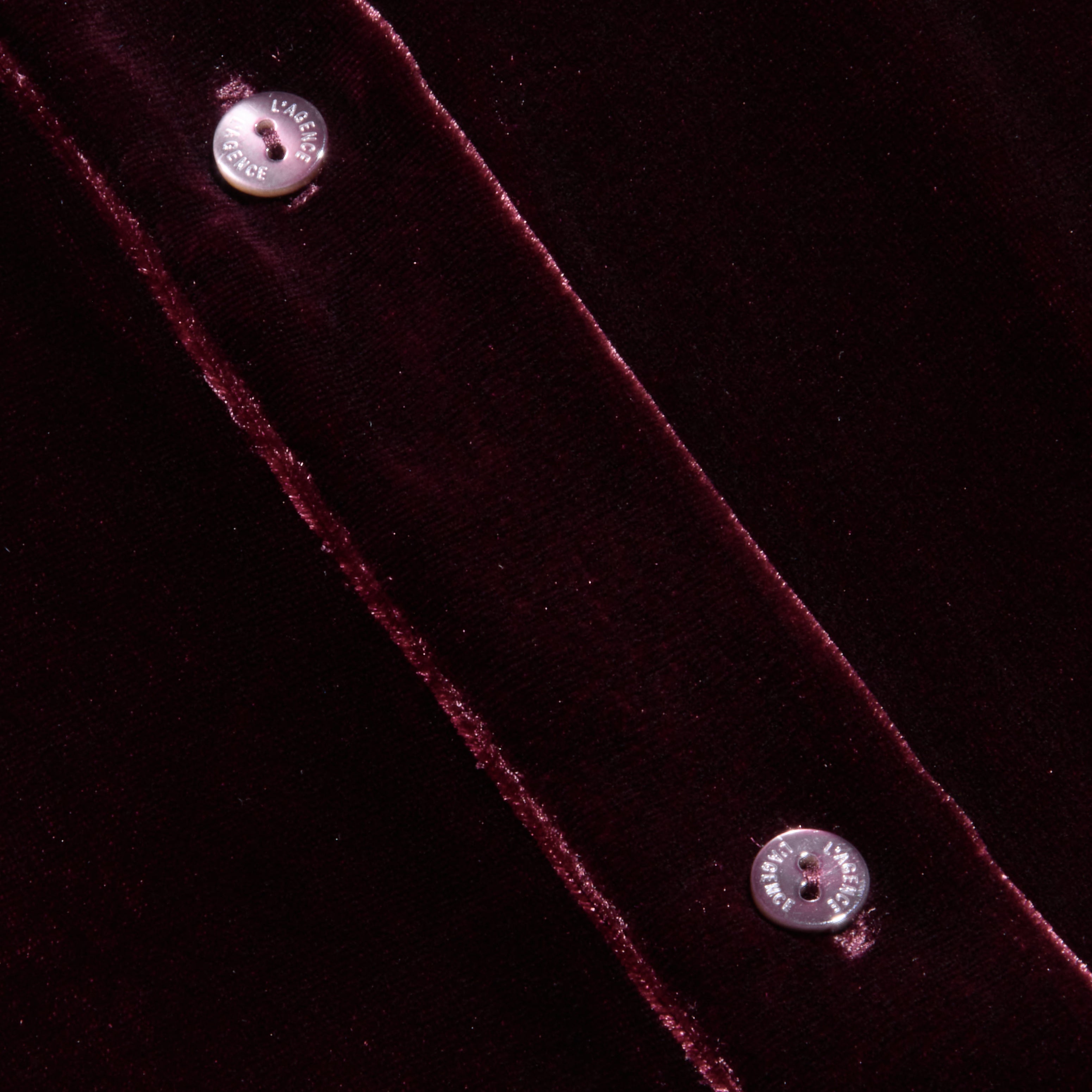 Close-up of the Cosette Velvet Shirt in dark red, featuring two silver snap buttons along a seam and highlighting the luxurious texture and sheen of the velvet fabric.