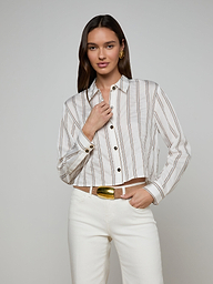 A woman wears the Cosette Shirt with jacquard stripes, paired with white pants, standing against a plain background—one hand near her collar and the other relaxed by her side.