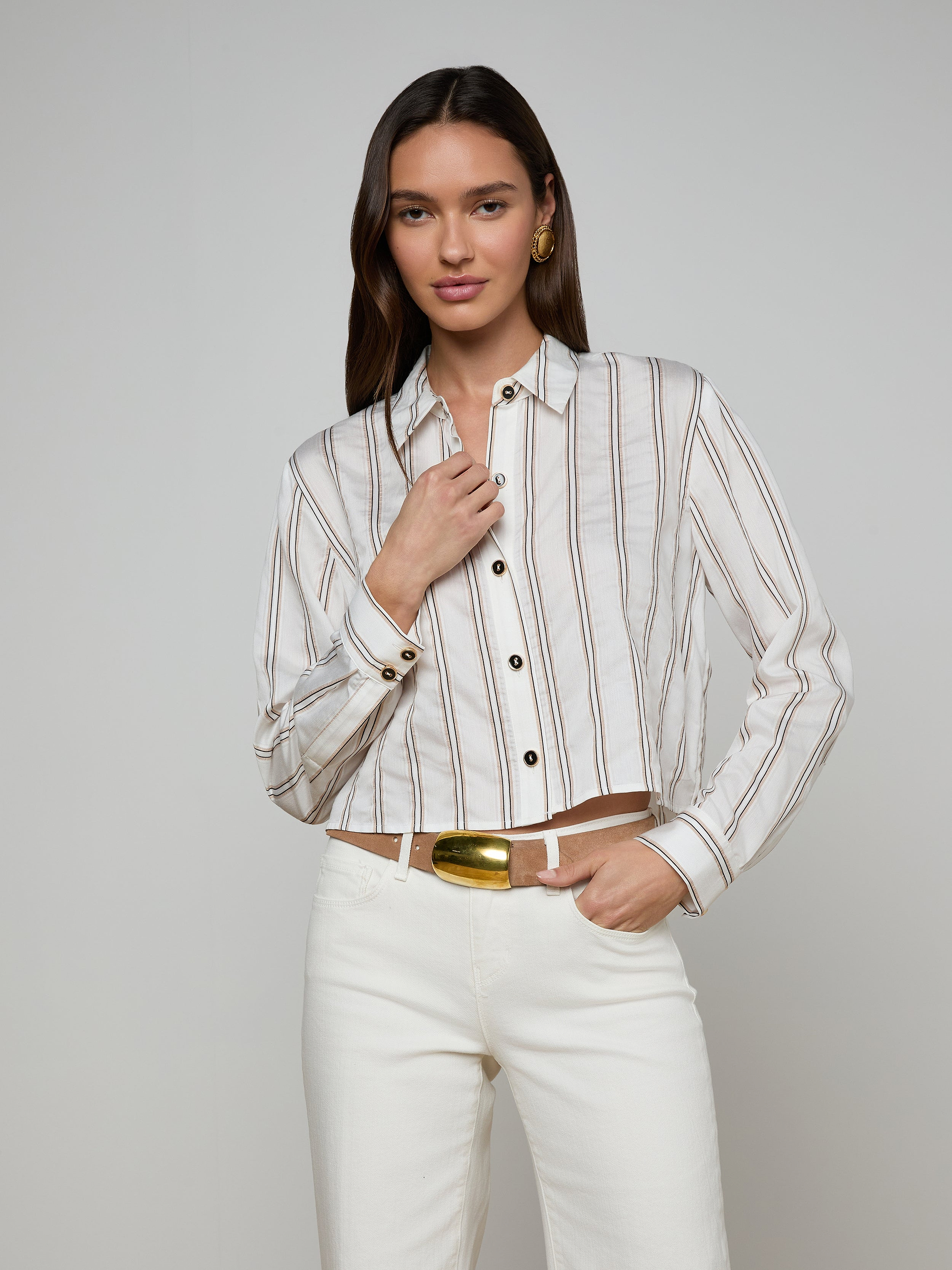 A woman wears the Cosette Shirt with jacquard stripes, paired with white pants, standing against a plain background—one hand near her collar and the other relaxed by her side.