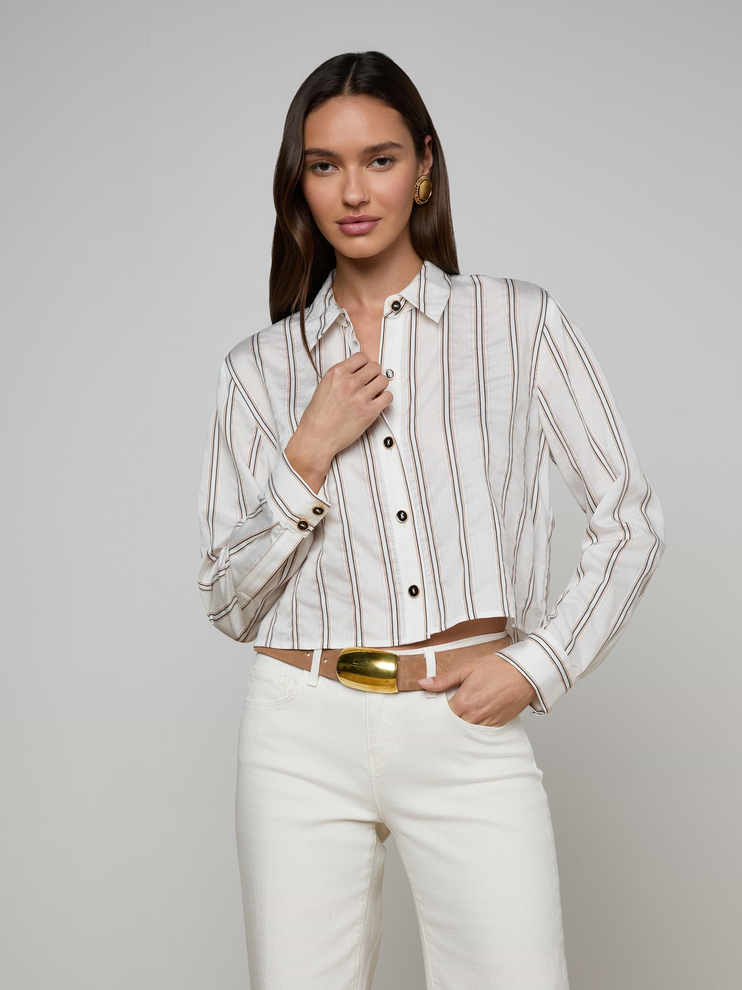 A woman wears the Cosette Shirt with jacquard stripes, paired with white pants, standing against a plain background—one hand near her collar and the other relaxed by her side.