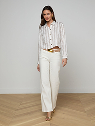 A woman wearing the Cosette Shirt with jacquard stripes, white wide-leg pants, a gold belt, and sandals stands against a plain white background. She has straight dark hair.