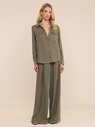 A woman stands against a white background wearing the Pearson Shirt, a lightweight lyocell button-down in smoky olive green, paired with matching wide-leg pants. She has long blonde hair and looks at the camera with a neutral expression.