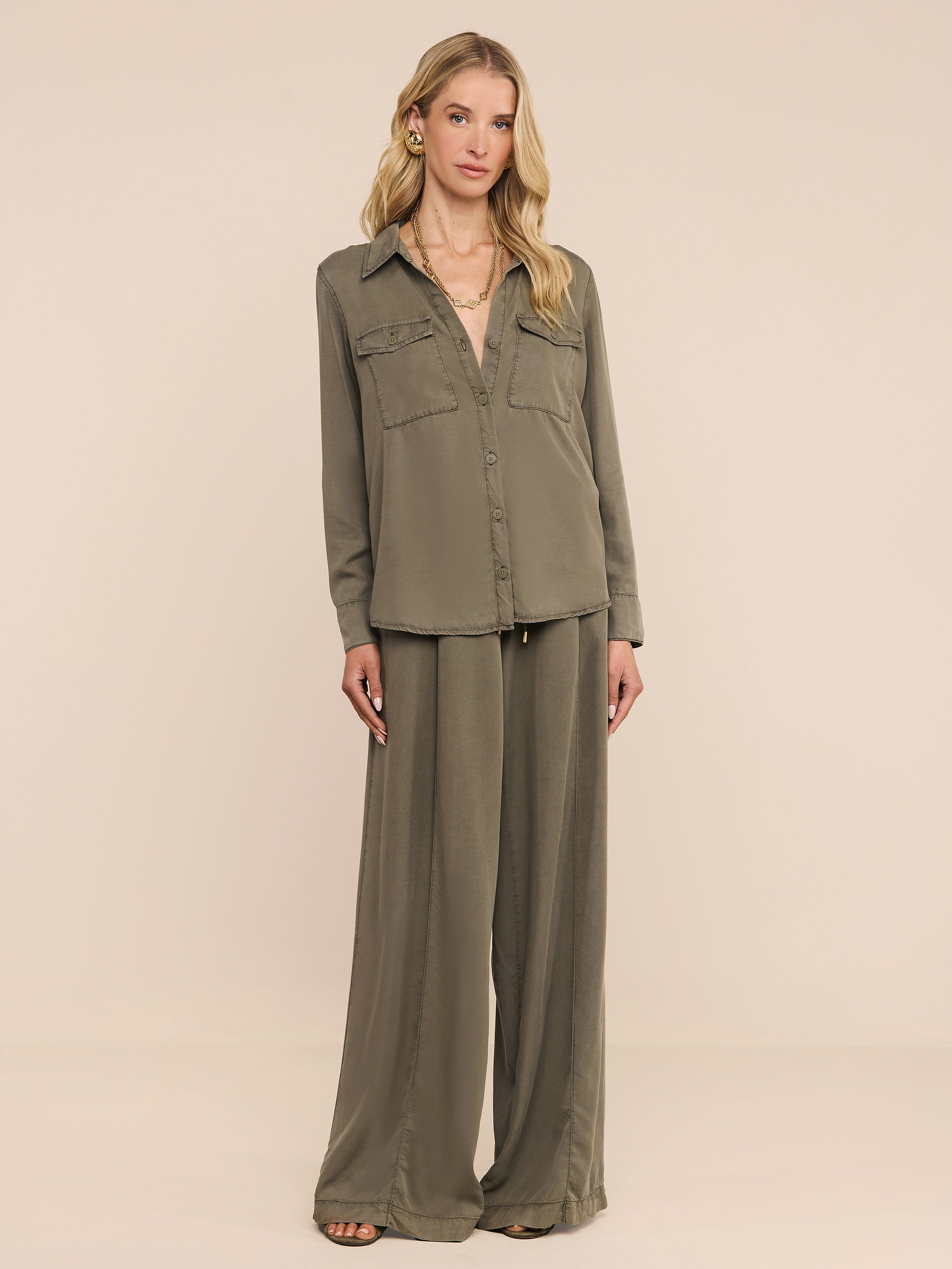 A woman stands against a white background wearing the Pearson Shirt, a lightweight lyocell button-down in smoky olive green, paired with matching wide-leg pants. She has long blonde hair and looks at the camera with a neutral expression.