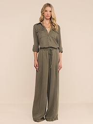 A woman stands facing forward, wearing the Pearson Shirt—a loose-fitting, button-down top crafted from lightweight lyocell in smoky olive green—with rolled-up sleeves, against a plain white background.