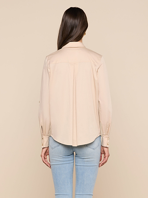 A woman with long brown hair wearing the Pearson Poplin Blouse and light blue jeans faces away from the camera against a plain beige background.