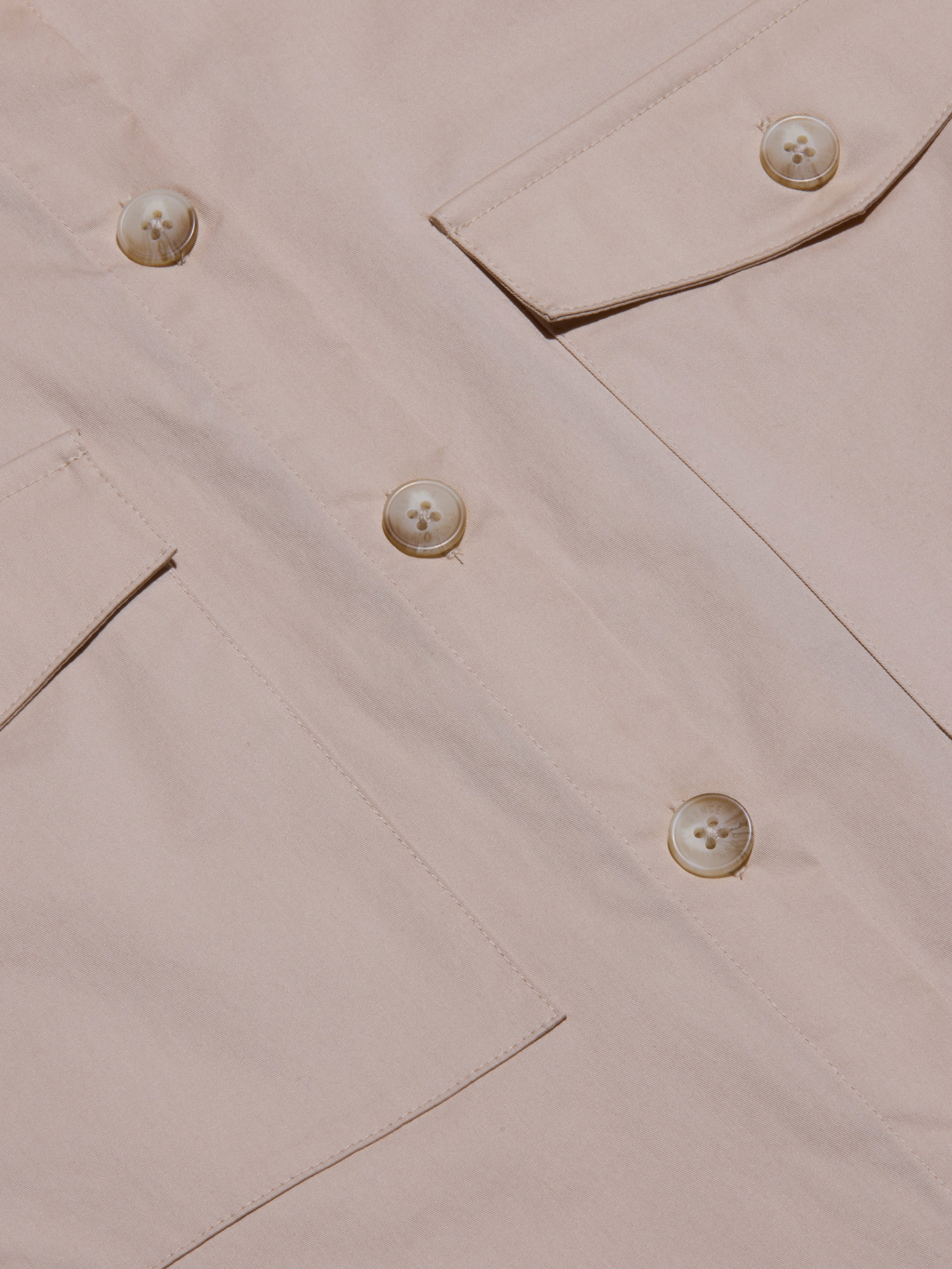 Close-up of the Pearson Poplin Shirt in light beige, featuring large buttons and two angled flap pockets, with a focus on the utility-inspired design, fabric texture, and detailed stitching.