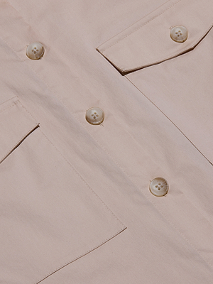 Close-up of the Pearson Poplin Blouse, a light beige utility-inspired button-down shirt with four buttons and two front flap pockets, highlighting its fabric texture and stitching details.