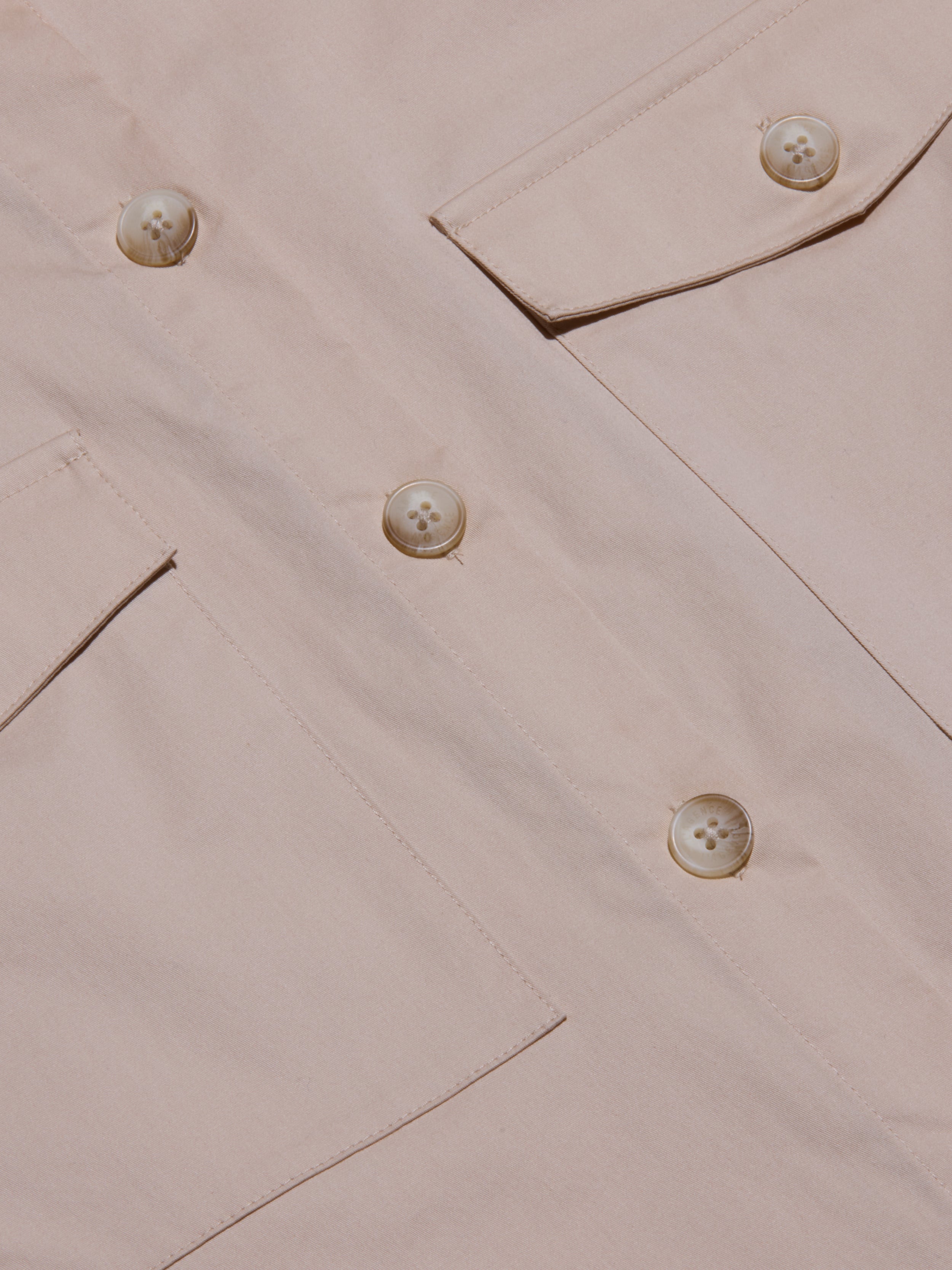Close-up of the Pearson Poplin Shirt in light beige, featuring large buttons and two angled flap pockets, with a focus on the utility-inspired design, fabric texture, and detailed stitching.