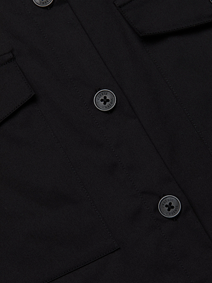 Close-up of the Pearson Poplin Shirt in black, showcasing two black buttons, partial views of two flap pockets, and visible stitching along the fabric.
