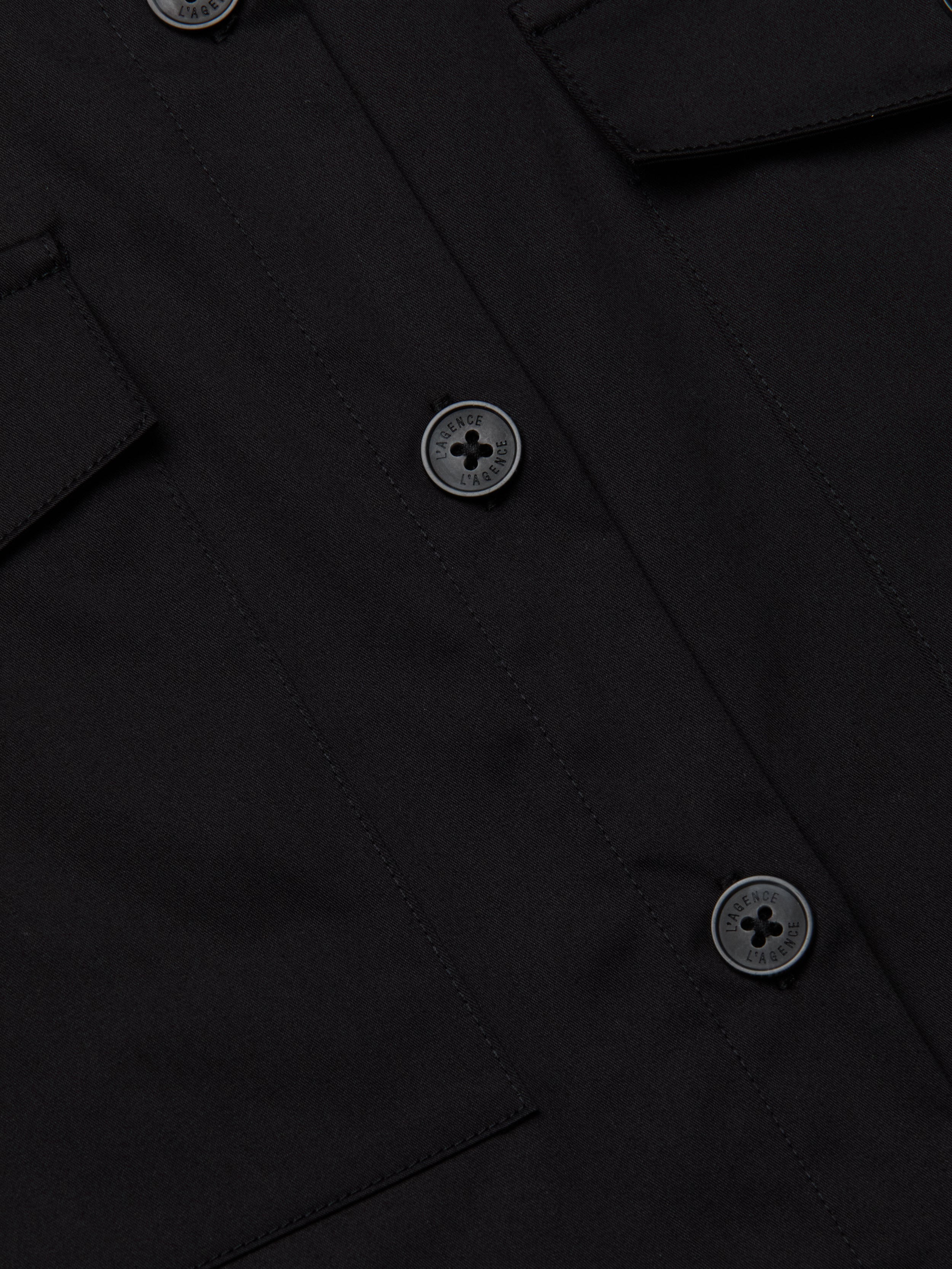 Close-up of the Pearson Poplin Shirt in black, featuring three round buttons and two flap pockets on either side.