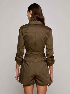 A woman with long brown hair, wearing gold hoop earrings and the Pearson Blouse by L'AGENCE Sale, stands facing away from the camera against a plain light gray background.