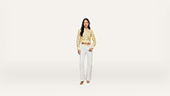 A woman stands against a plain white background, wearing a yellow long-sleeve crop top with lace details and high-waisted white wide-leg pants, completed with light-colored sandals.