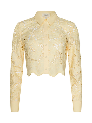 The Seychelle Cropped Eyelet Blouse is a light yellow, long-sleeve, collared top with floral eyelet patterns, scalloped hem, front buttons, a semi-sheer poplin lace design, cropped fit, and L’AGENCE label inside the collar.