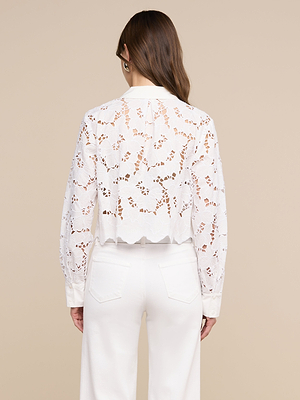 تظهر امرأة ذات شعر بني طويل من الخلف، وهي ترتدي بلوزة «Seychelle Cropped Eyelet» وسروالاً أبيض على خلفية بيج.