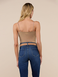 A woman with long blonde hair is shown from the back, wearing the Gelina Mesh Bodysuit—a tan spaghetti strap top with a scoop neckline—paired with blue jeans, standing against a plain, light background.
