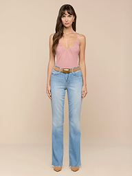 Une femme est de face, vêtue de la combinaison Gelina Mesh Bodysuit en rose avec des bretelles réglables, dun jean bleu clair à taille haute, dune ceinture beige et de talons beiges sur un fond beige uni.