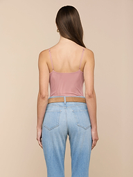Une femme aux longs cheveux bruns se tient de face, vêtue de la combinaison Gelina Mesh Bodysuit à bretelles réglables et dun jean bleu clair à taille haute, sur fond beige.