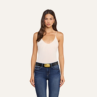 A woman with long brown hair wears the Gelina Mesh Bodysuit—a sleeveless, light pink bodysuit with adjustable straps—paired with blue jeans and a black belt. She stands facing forward against a plain white background.