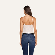 Si vede di spalle una donna dai lunghi capelli castani che indossa il body Gelina Mesh con spalline regolabili, abbinato a jeans blu con tasche posteriori e una cintura nera testurizzata, in piedi su uno sfondo beige.