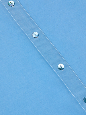 Close-up of the Marlene Blouse’s light blue fabric, showcasing a diagonal strip with white stitching and four shiny silver buttons—ideal details for this lightweight button-down.