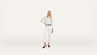 Woman standing confidently in all-white attire, including a button-up shirt and cropped pants, with black heels and a black belt, against a plain white background.