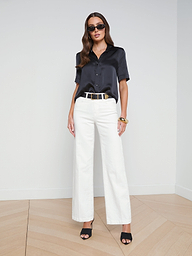 Wearing the Ellah Silk Blouse styled for a chic summer look, a woman pairs it with white wide-leg pants, black heels, a black belt, and sunglasses as she stands against a plain white background.
