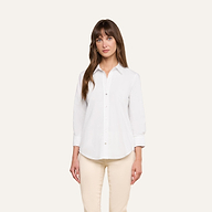 A woman with long brown hair stands against a plain light background, facing forward with a neutral expression, wearing the Daniella Cotton-Blend Blouse in white with three-quarter sleeves and cream pants.