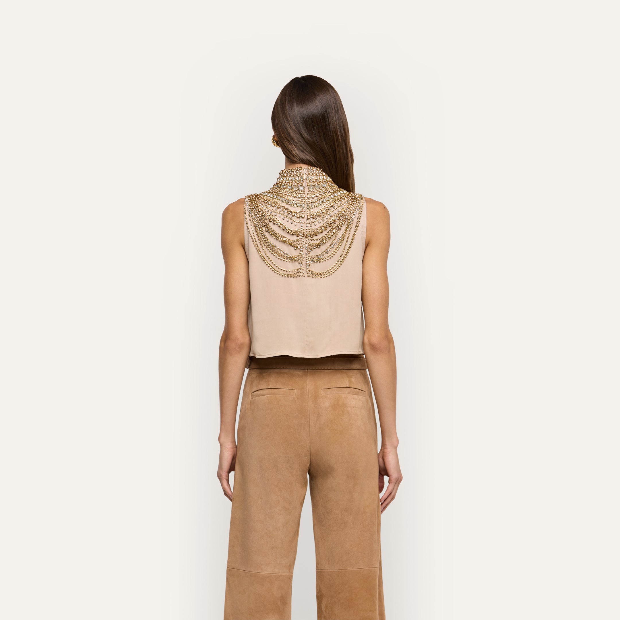 The Yun Crystal Tank is a beige sleeveless top featuring an ornate gold chain embellishment draped across the back of the neck and shoulders.