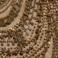The Yun Crystal Tank features rows of gold-toned chains dripping with faceted crystals arranged in curved patterns on beige fabric.