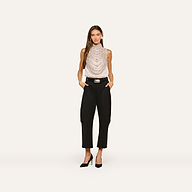 A woman stands against a plain background wearing the Yun Draped Crystal Tank styled with layered necklaces, black belted pants, and black heels, her hands in her pockets.