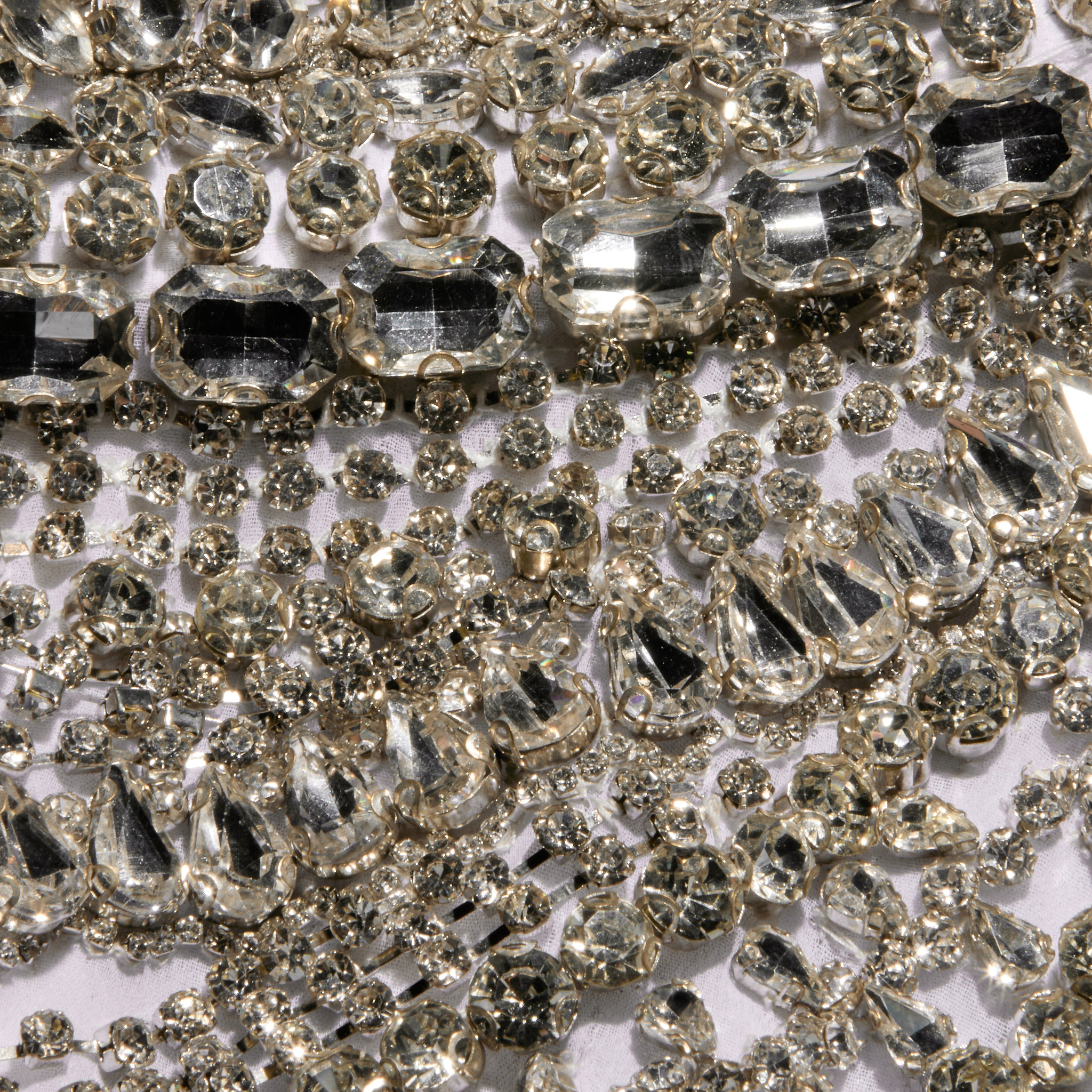 A close-up of numerous sparkling, clear rhinestones of various shapes and sizes clustered together on a reflective surface, evoking the dazzling embellishments of the Yun Draped Crystal Tank—an ideal choice for a festive holiday party.
