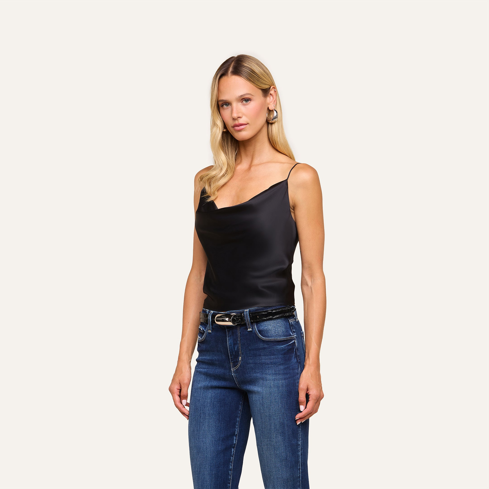 A woman with long blonde hair wears the Calista Silk Camisole in black and blue jeans, standing against a plain light background.