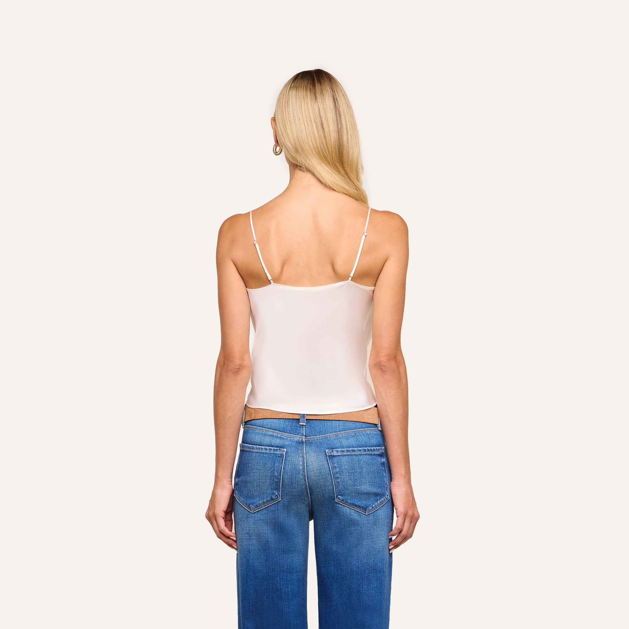 A woman with long blonde hair is seen from the back in the Calista Silk Camisole and blue jeans, standing against a plain light background.