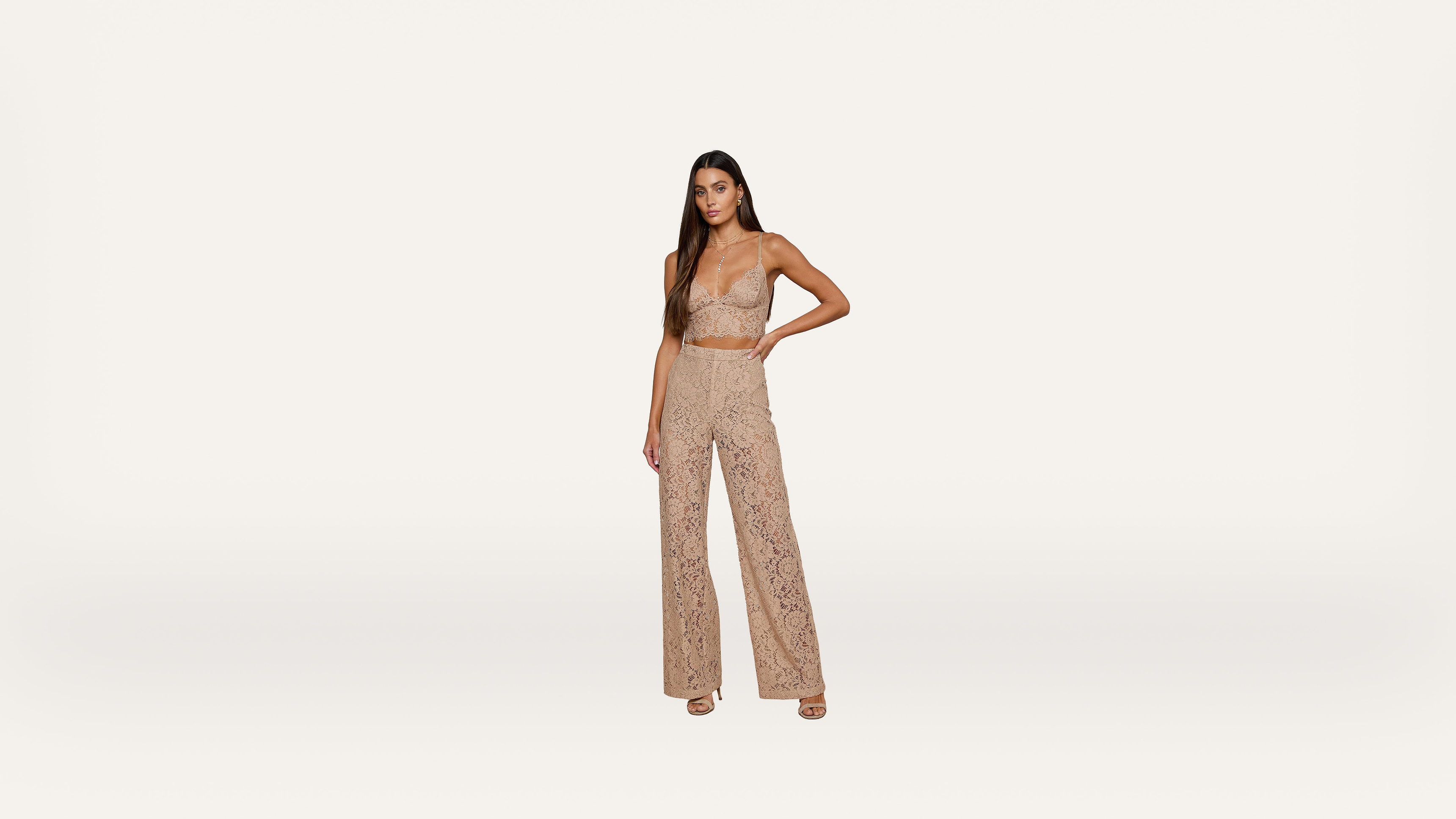 Woman wearing a tan, lace crop top and matching high-waisted lace pants, standing against a plain white background.
