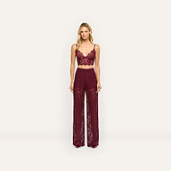 A model wears the Aislin Lace Bralette in dark red sheer stretch lace with adjustable straps, paired with high-waisted wide-leg pants.